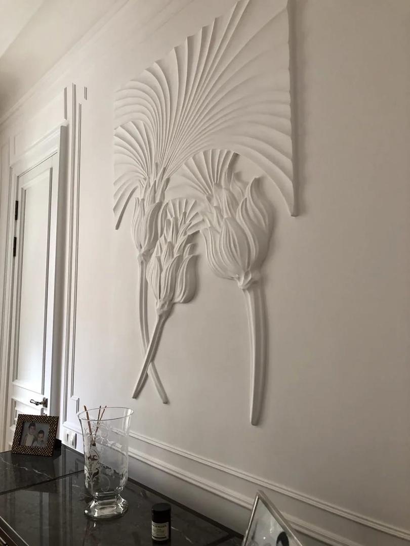 Sculpted artichoke and fan-leaf reliefs installed on a pale wall.