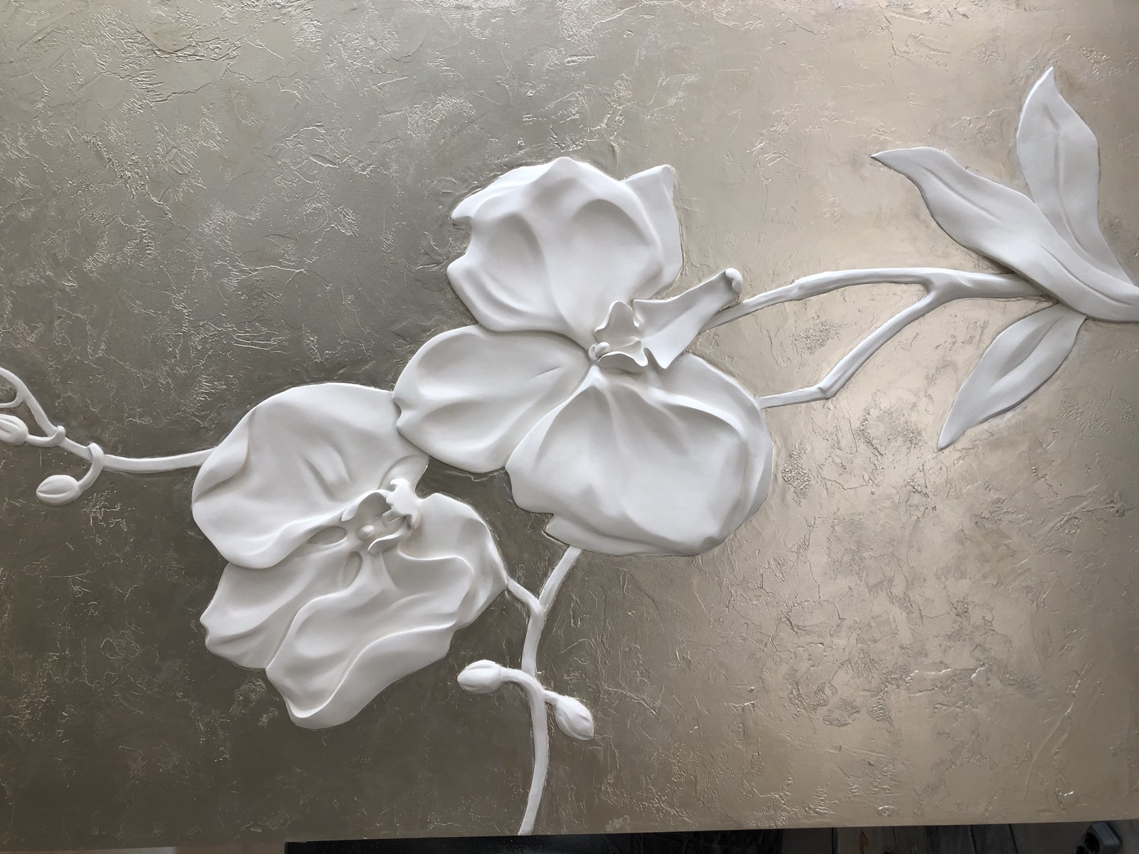 Two white sculpted orchids in relief against a metal-leaf panel.